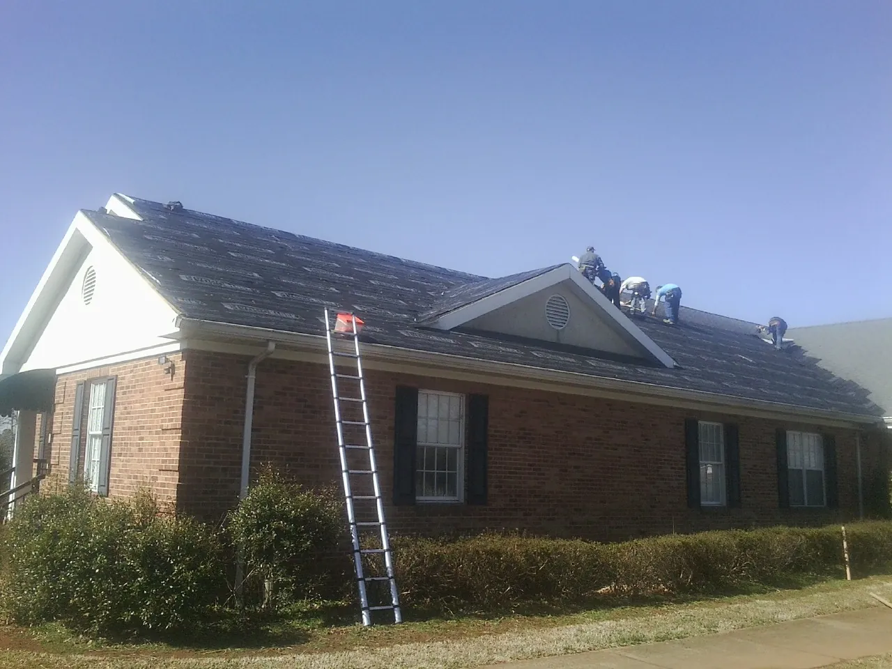 Crew tearing shingles off a brick ranch roof with a ladder set — Metal Roof Repair work by our crew in Waccabuc