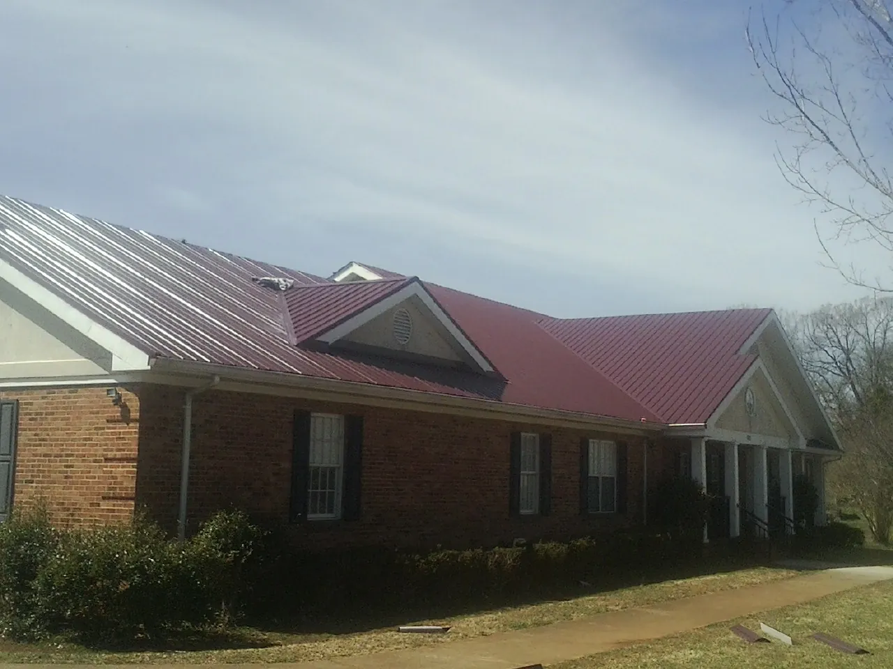 Red metal roof with gabled entries on a long brick building, from a Hail Damage Roof Repair job in Waccabuc