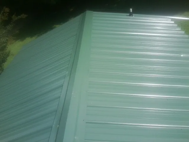 New green metal panels meeting at the ridge of a roof — Flat Roof Repair work by our crew in Waccabuc