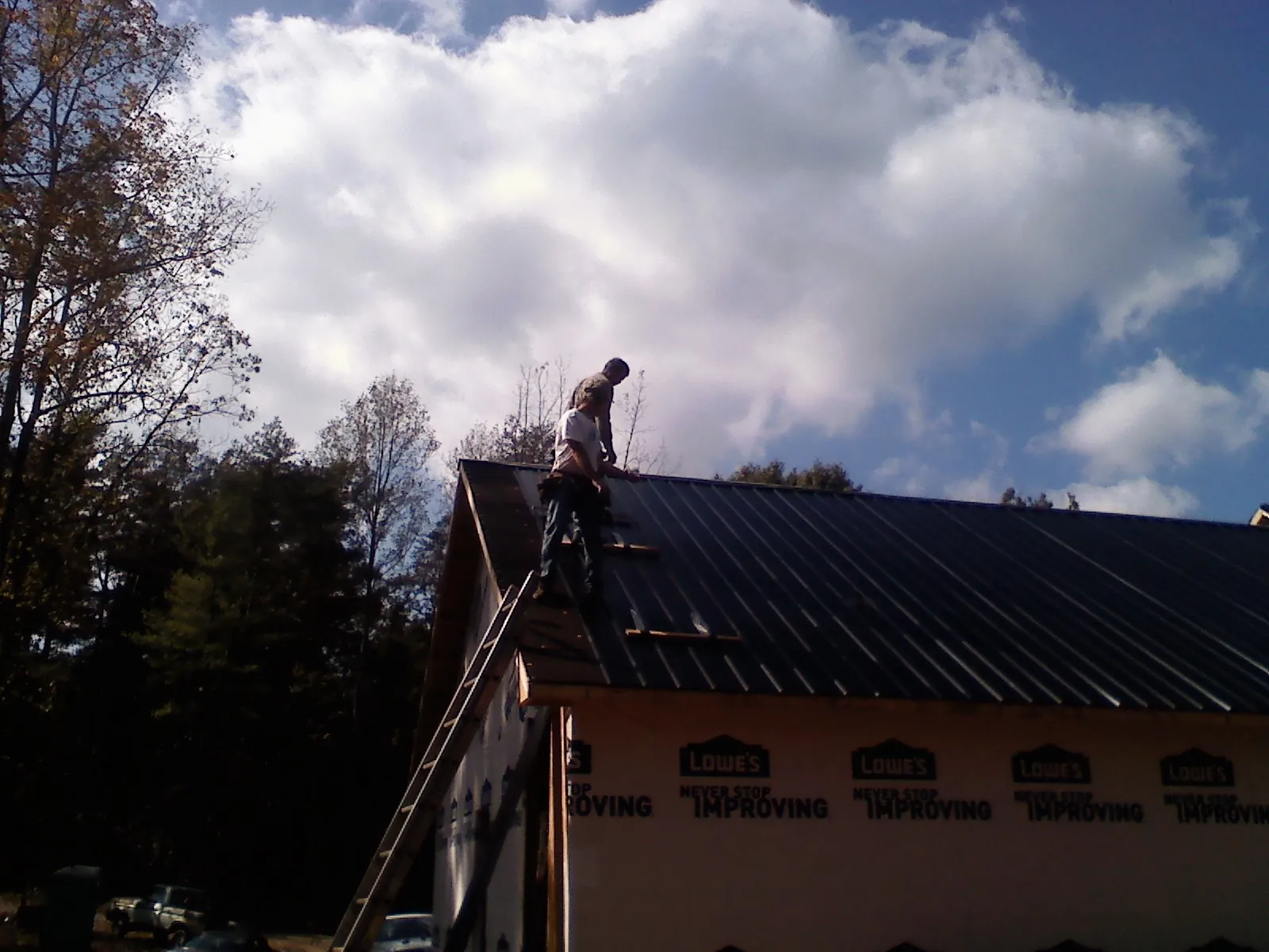 Roofer fastening dark metal panels high against a cloudy sky, from a Roof Inspection job in Waccabuc
