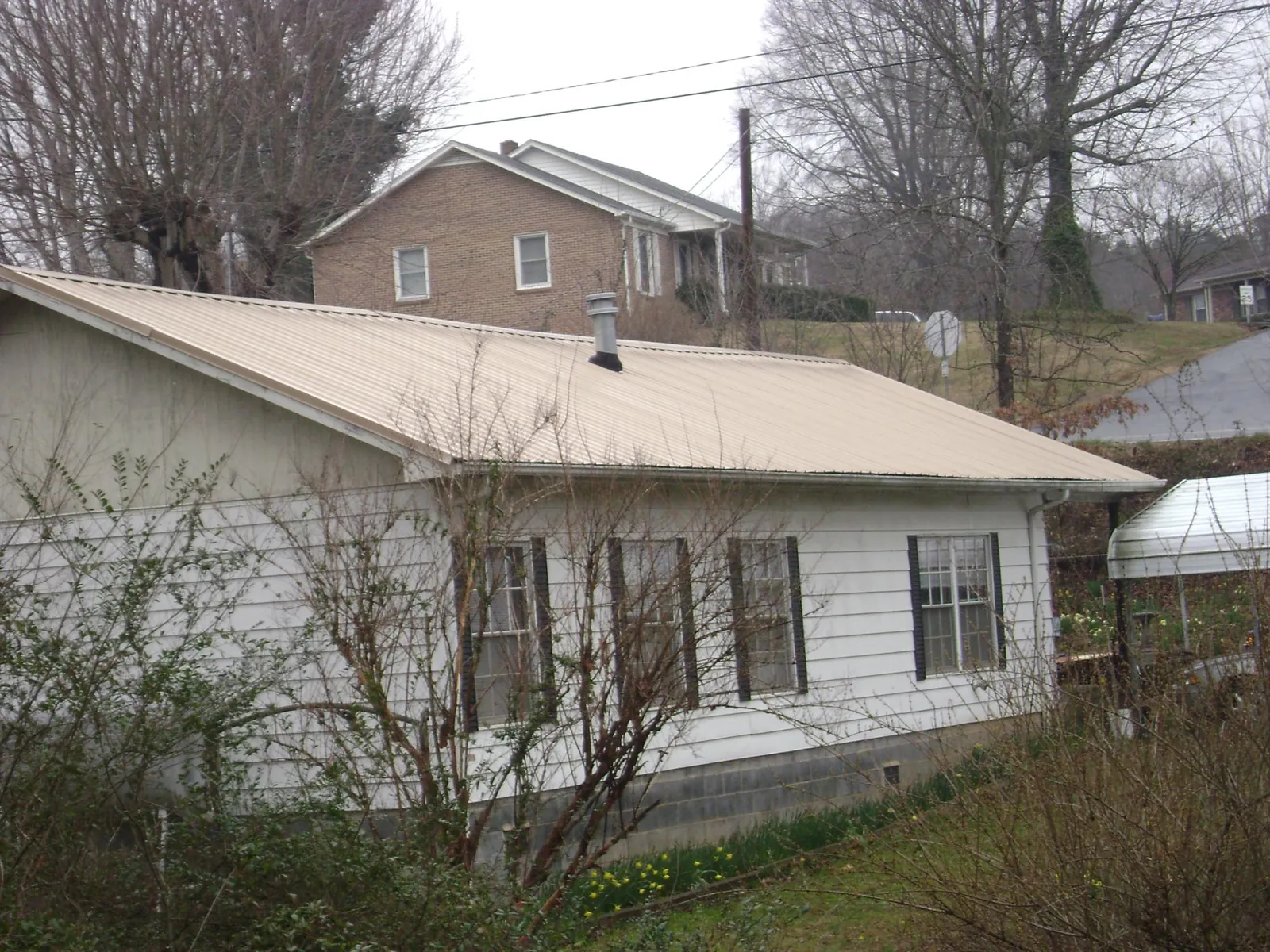 Tan metal roof on a white sided house set into a hillside — Commercial Roofing by Roofing Brothers in Waccabuc